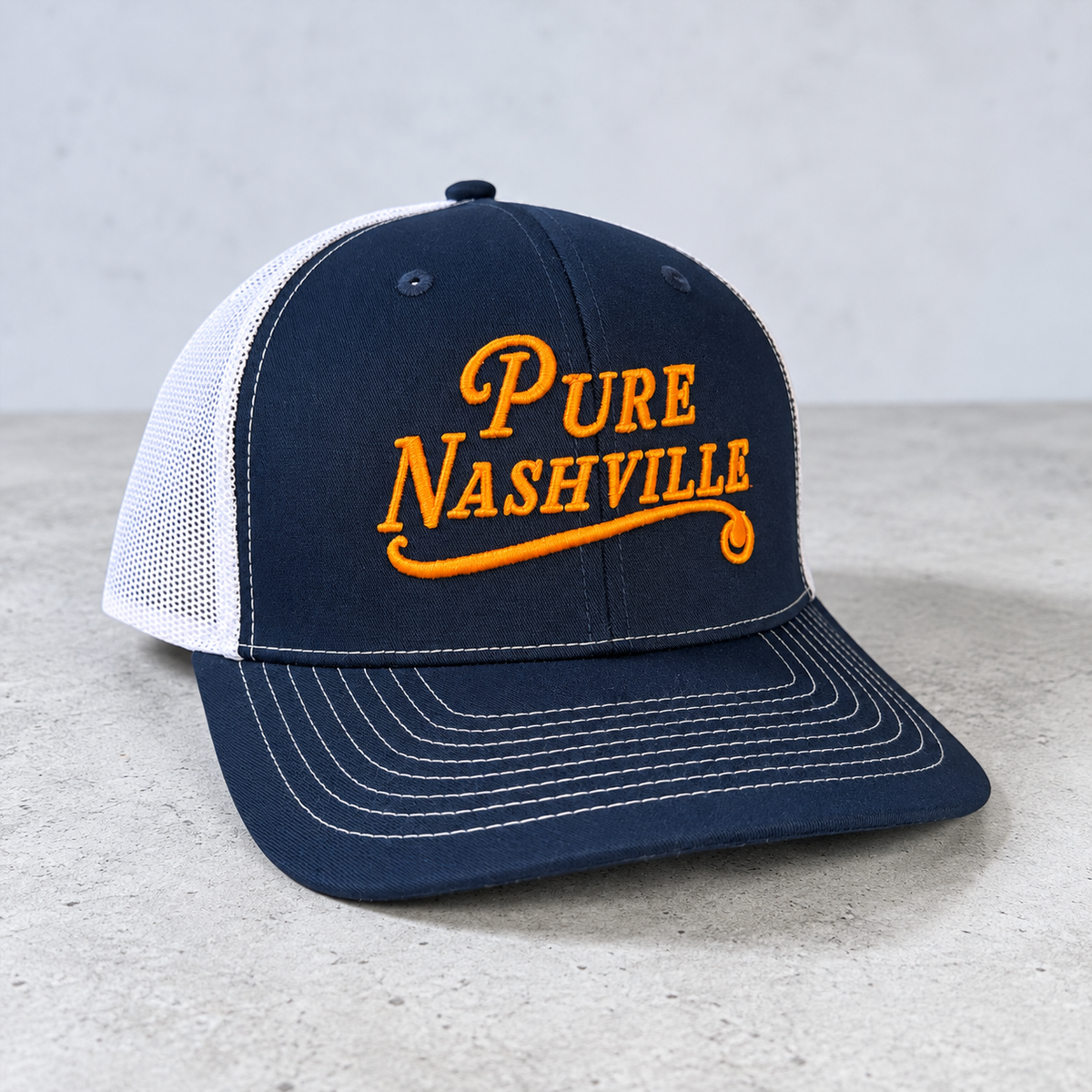 Navy and white mesh trucker hat with orange Pure Nashville embroidery
