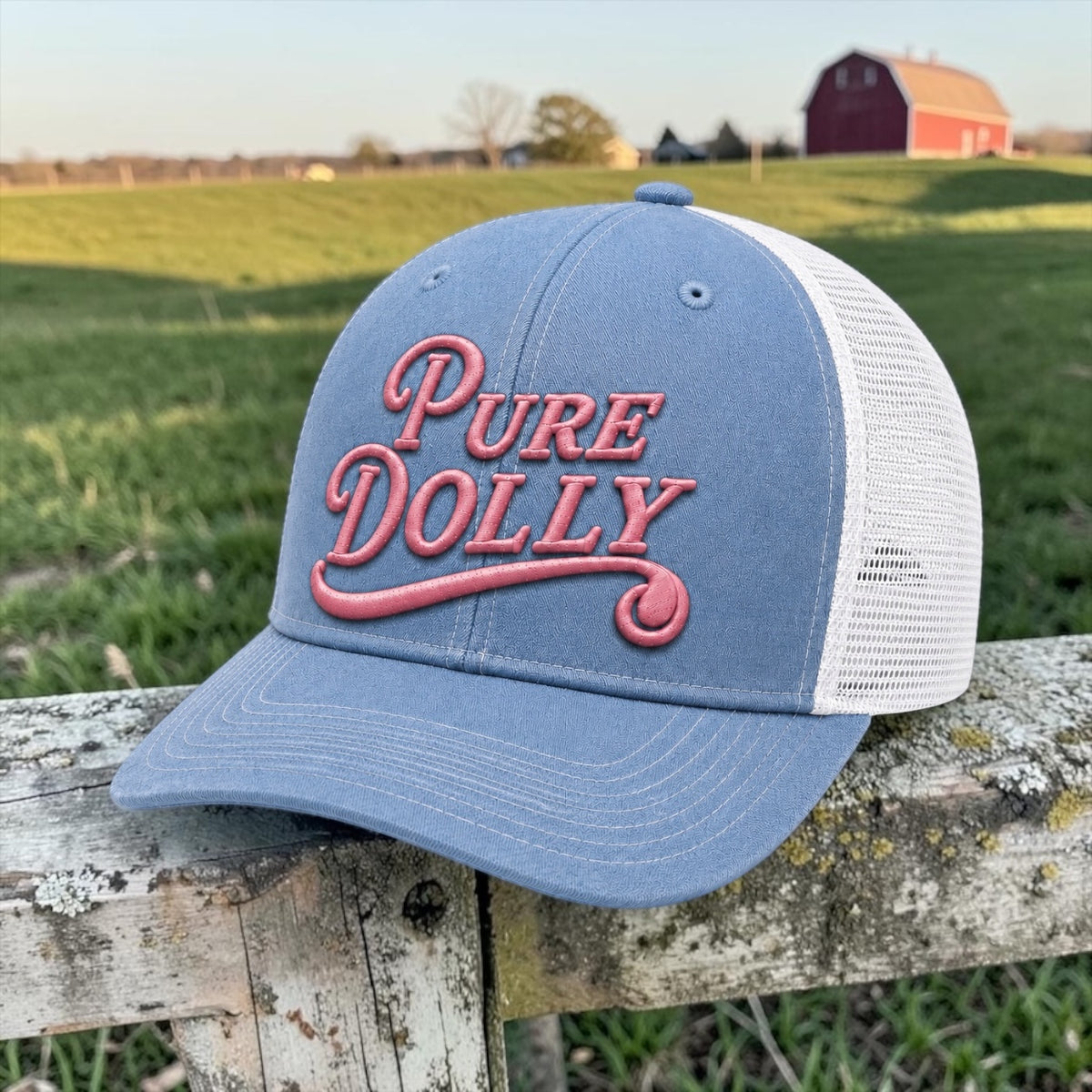 Pure Dolly Trucker Hat in Blue and White on a fence post with green field and red barn background