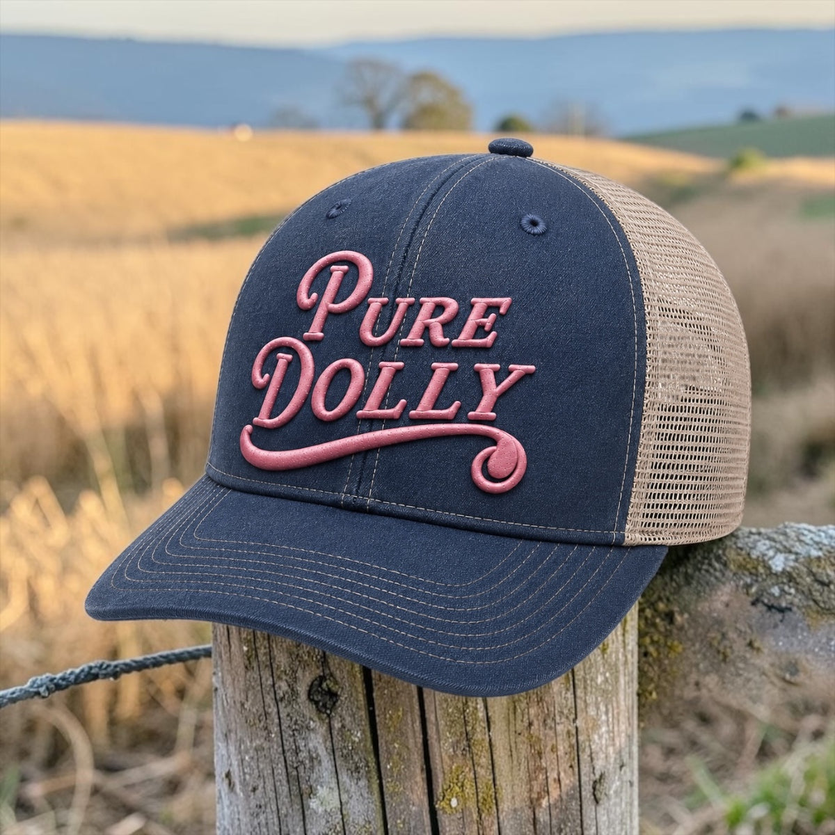 Pure Dolly Trucker Hat in Navy and Khaki on a fence post with golden field background