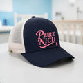 Pure NICU Trucker Hat in Navy and White with pink puff embroidery, set in a hospital room